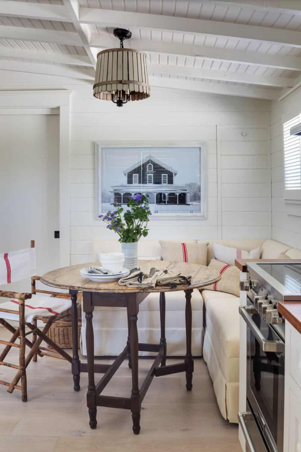 Cottage breakfast nook with antique gate-leg table, linen banquette, rope drum pendant, and black-and-white architectural print