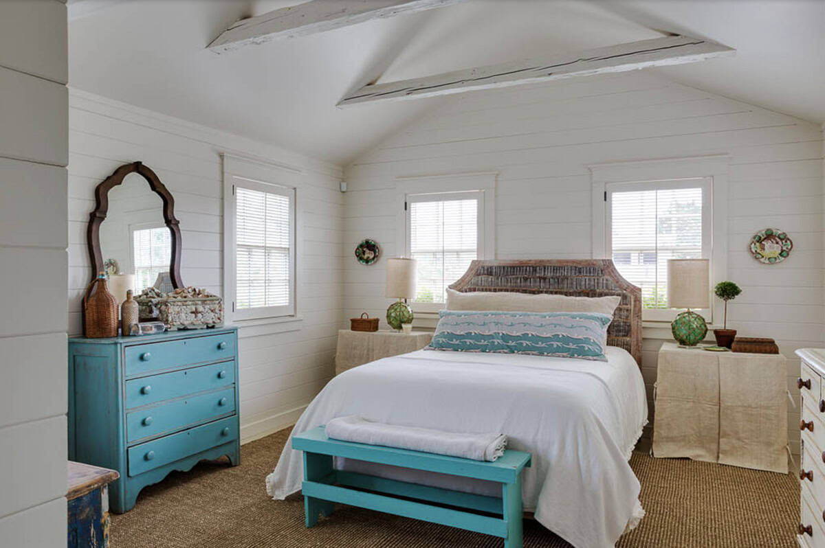 Bright cottage bedroom with vaulted ceiling, carved wood headboard, turquoise dresser, and seagrass rug