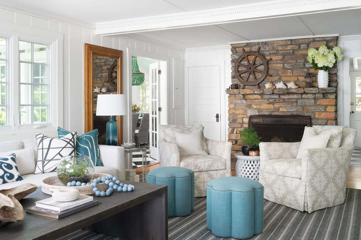 Coastal living room with stone fireplace, ship's wheel decor, teal ottomans, and gold leaning mirror