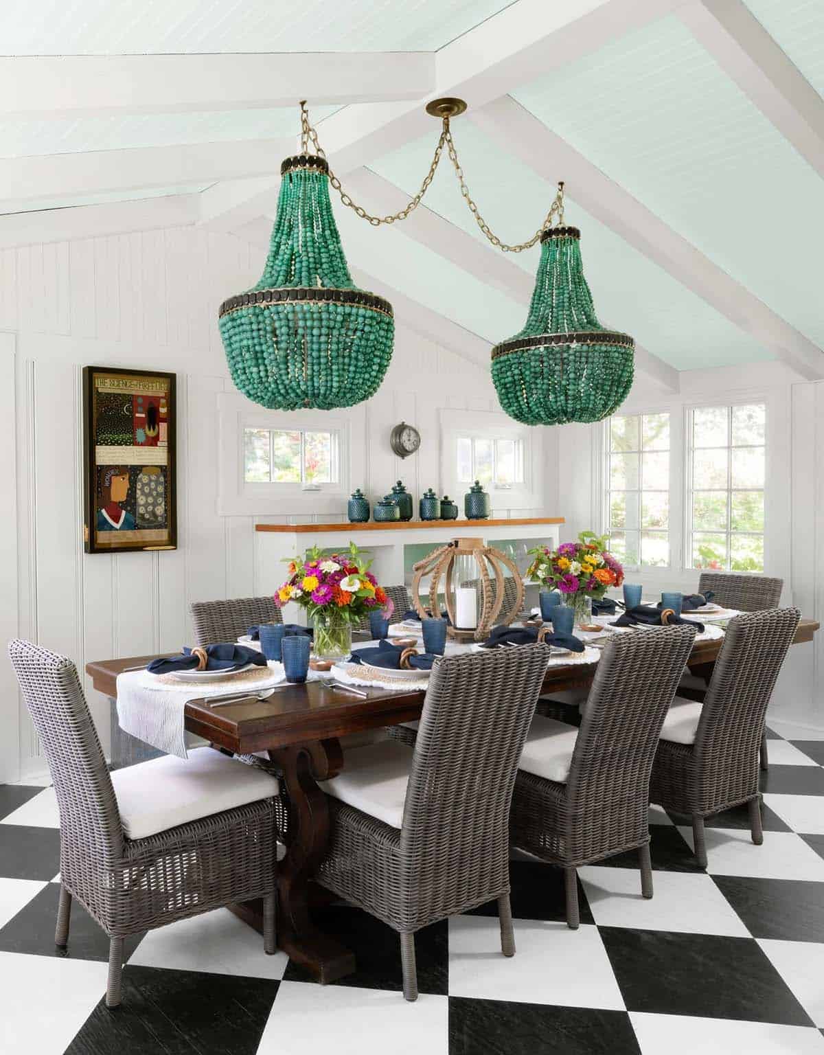 Dining room with a pair of green beaded chandeliers, wicker chairs, wood trestle table, and mint painted ceiling