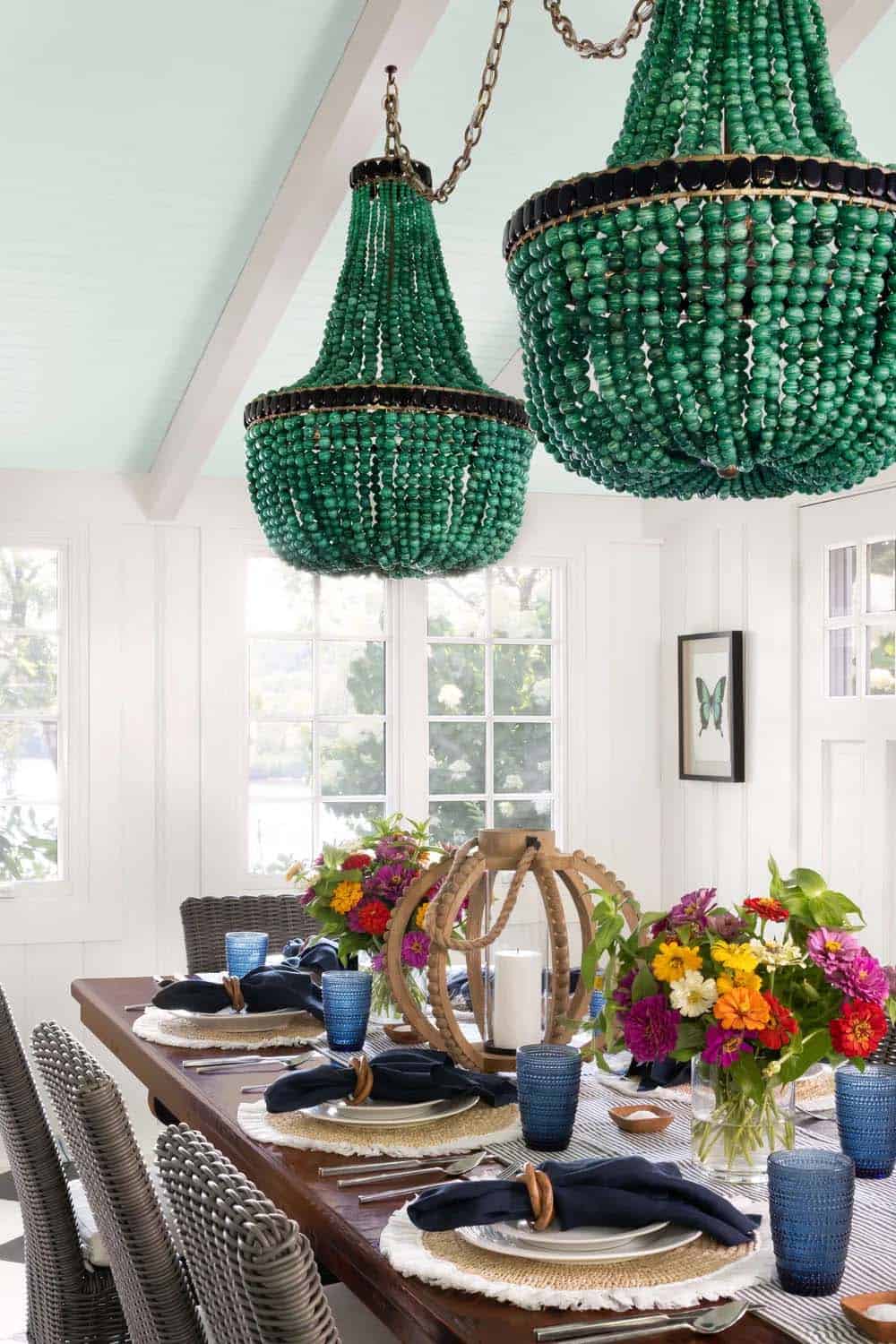 Close-up of pair of emerald green beaded empire chandeliers over set dining table with colorful flowers