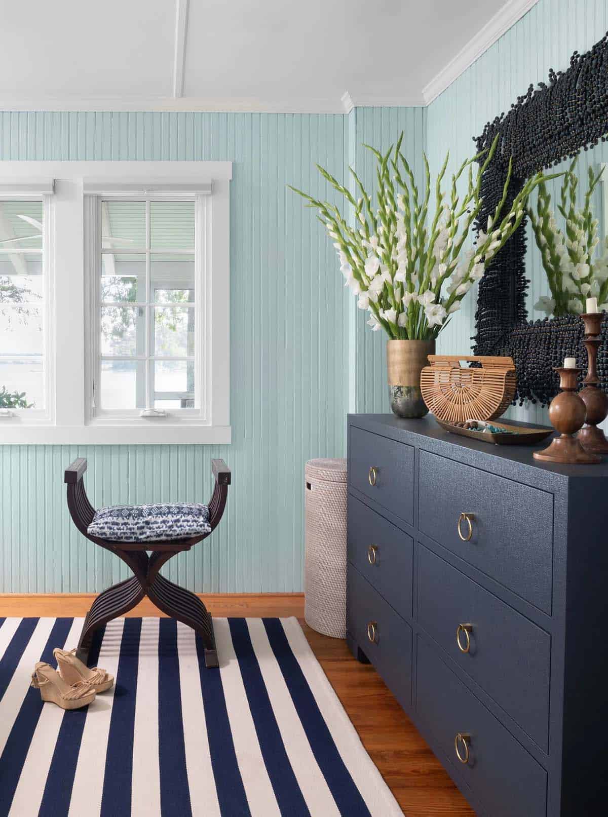 Bedroom corner with pale blue beadboard walls, navy grasscloth dresser, shell mirror, and gladiolus arrangement