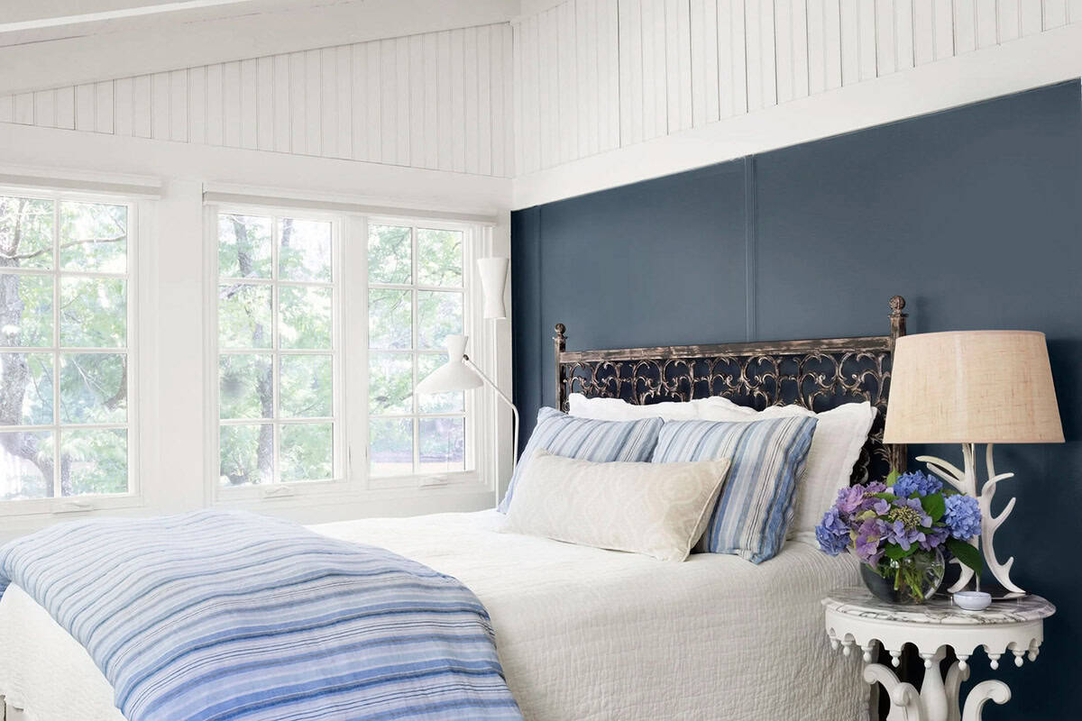 Primary bedroom with navy accent wall, ornate iron headboard, striped bedding, and tree-framed windows