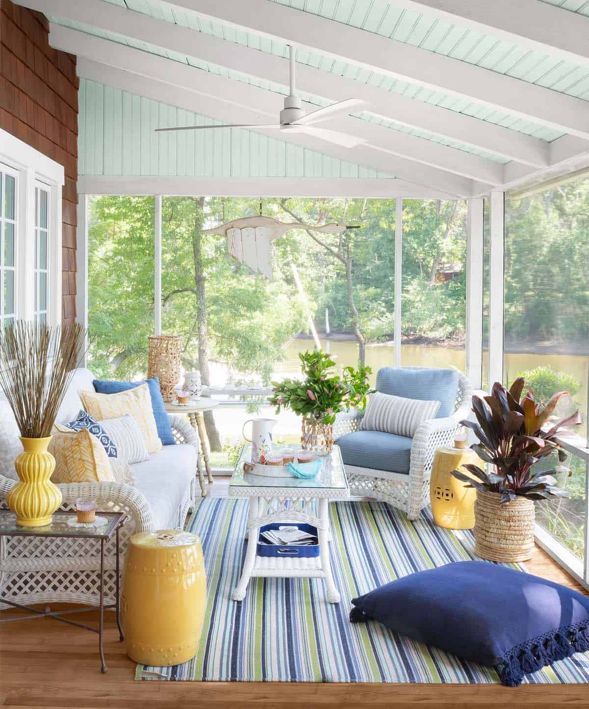 Screened porch with white wicker furniture, yellow garden stools, striped rug, and river views