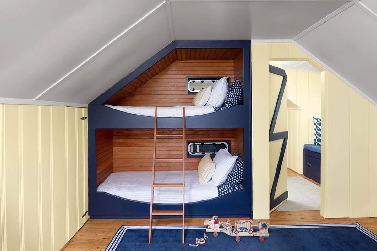 Built-in cedar bunk beds with navy trim, porthole windows, ladder, and yellow beadboard walls
