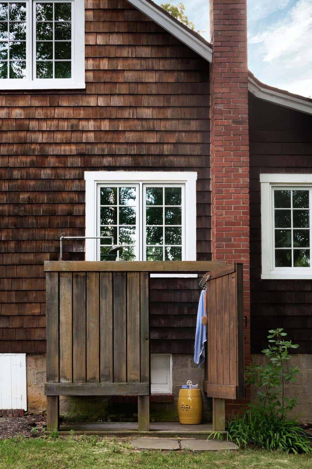 Cedar shake exterior with outdoor wood shower enclosure and yellow garden stool beside brick chimney