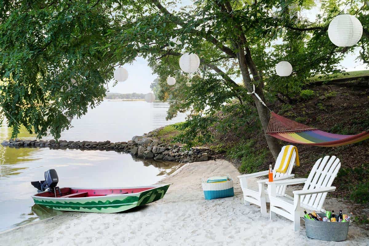 Sandy private beach with watermelon-painted boat, white Adirondack chairs, hammock, and paper lanterns in trees