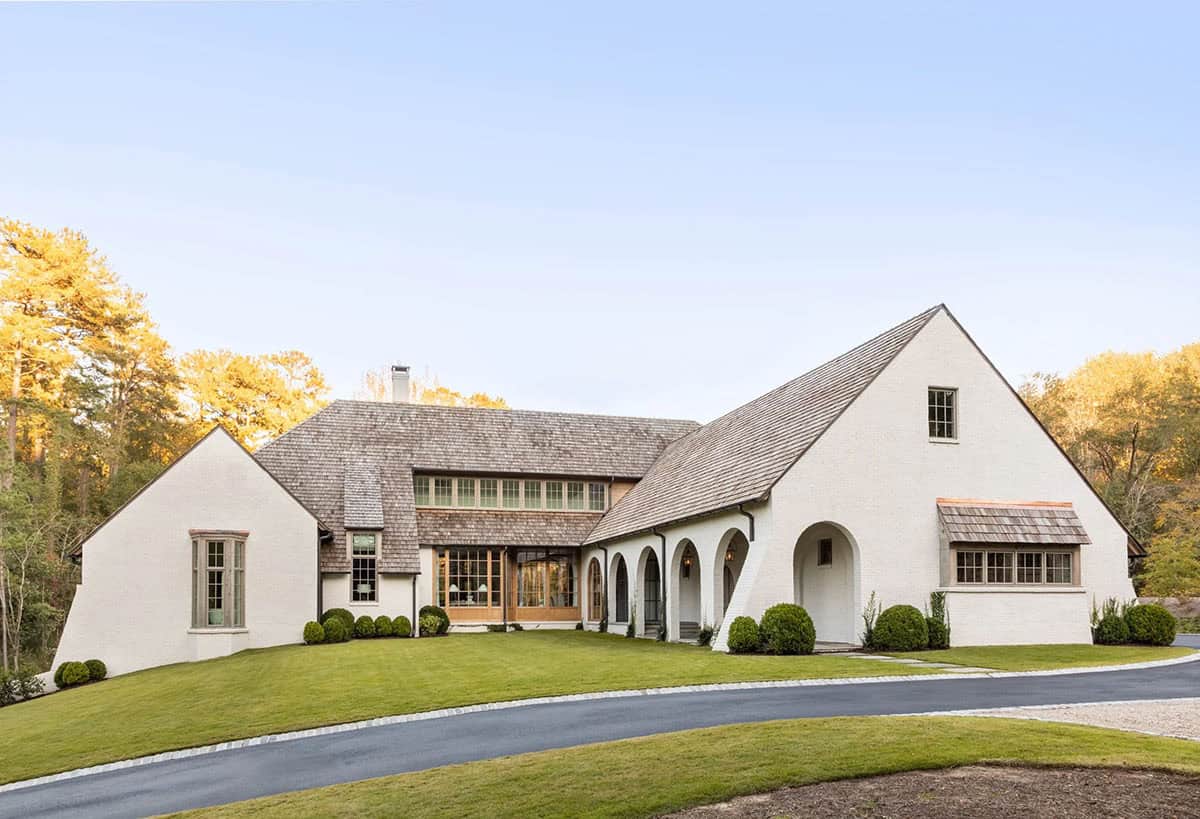 Wide-angle front exterior of white brick Belgian farmhouse home with cedar shake roof and stone path