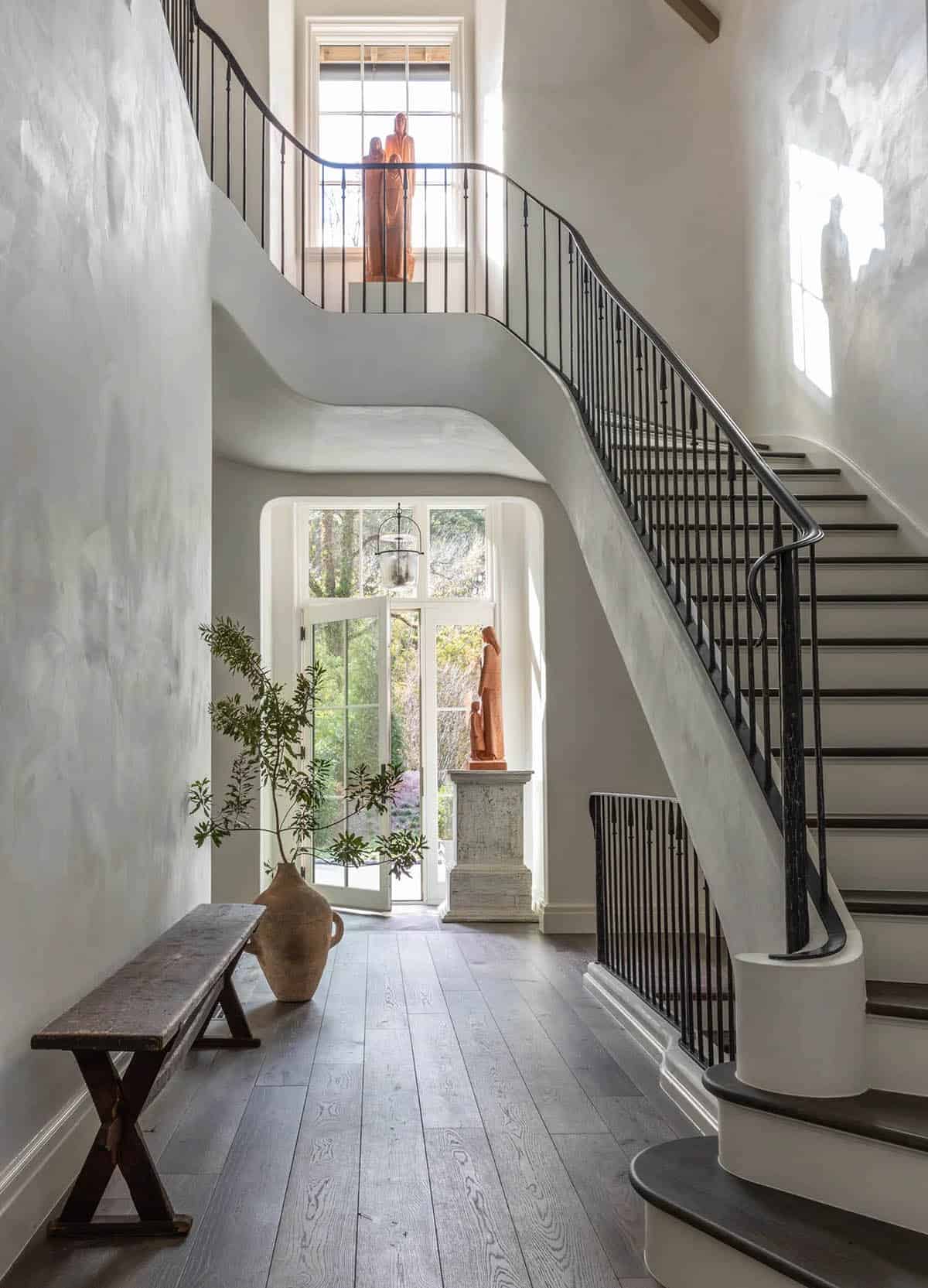 Two-story entry foyer with curved plaster staircase, iron balustrade, and terracotta sculpture