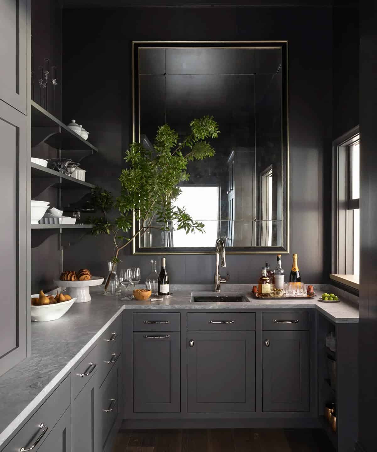 Moody dark butler's pantry with charcoal cabinetry, marble countertops, and antiqued mirror
