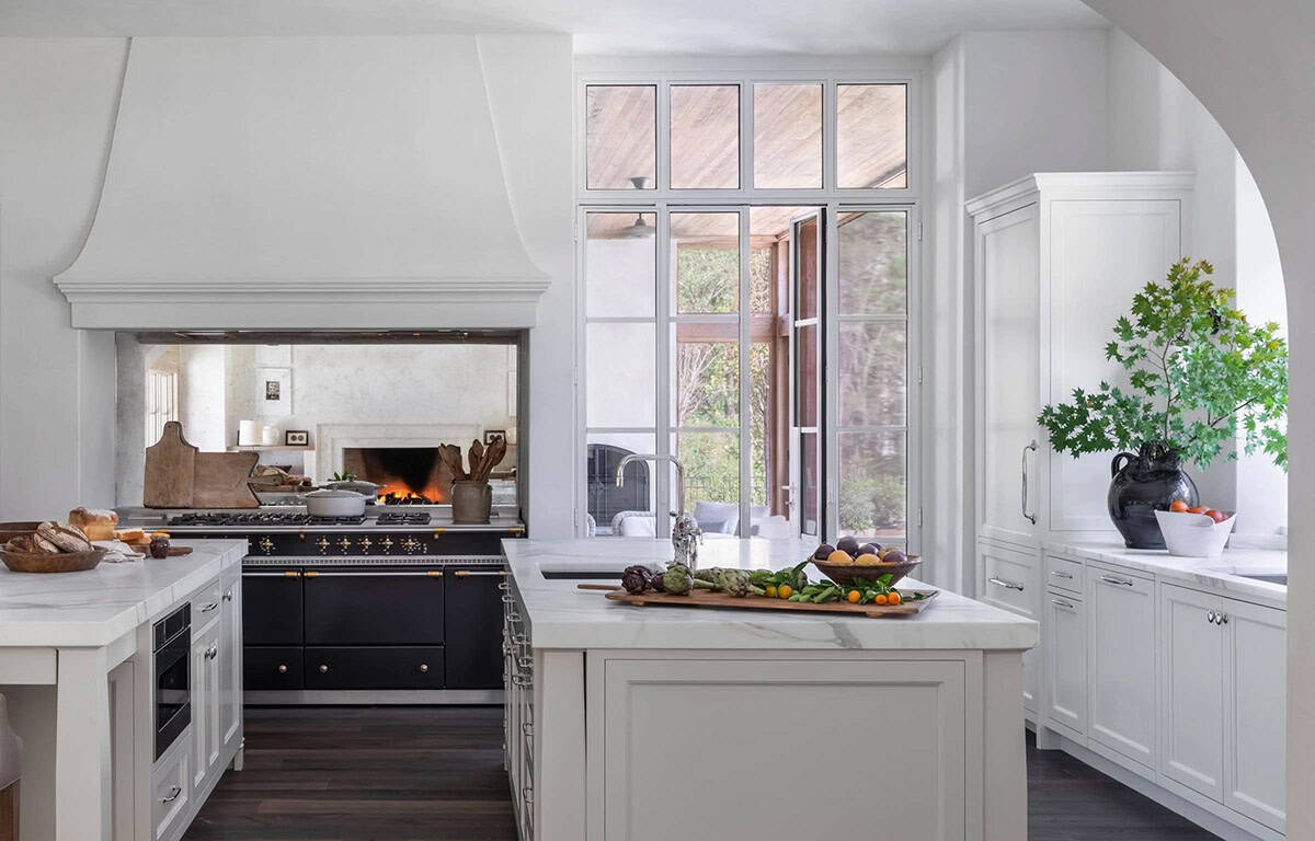 White kitchen with La Cornue range, plaster hood, marble island, and arched doorway