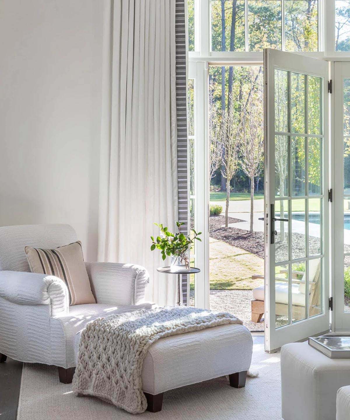 Bedroom sitting area with chaise lounge, chunky knit throw, and French doors to pool garden