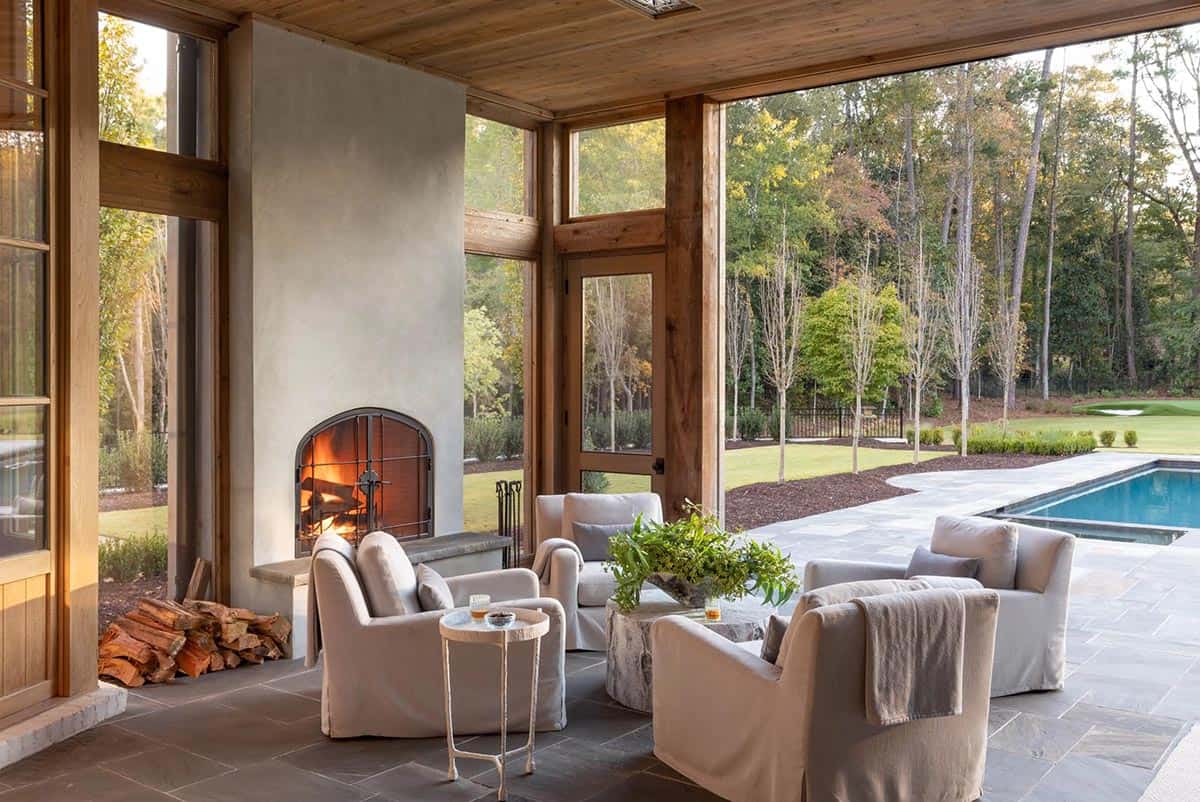 Screened outdoor living room with plaster fireplace, linen armchairs, and pool view beyond