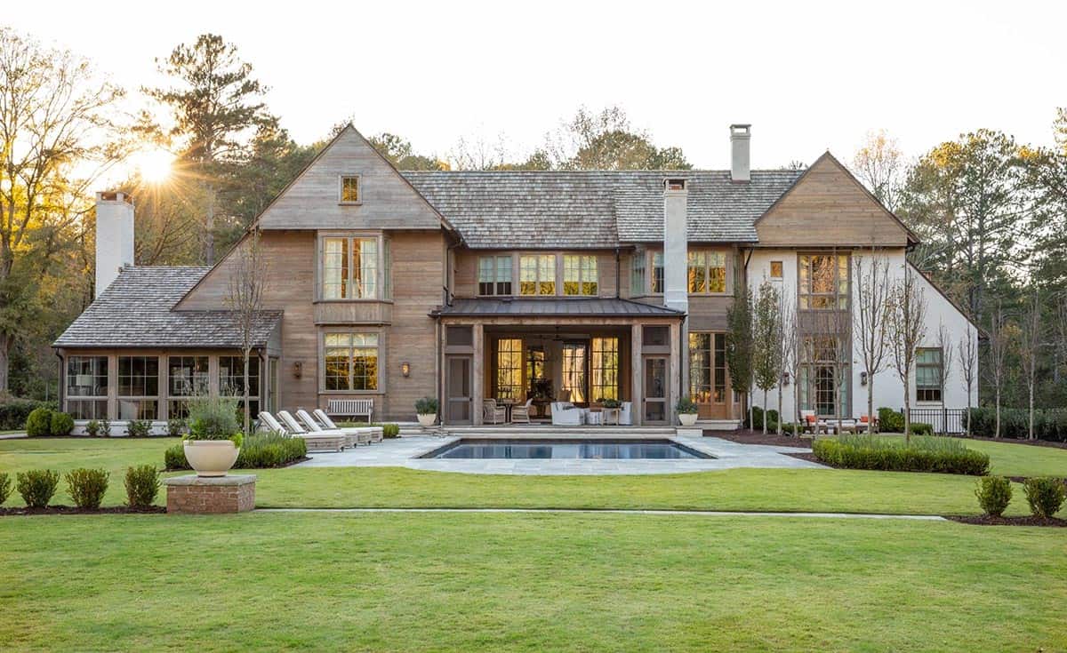 Rear exterior of Belgian farmhouse home at sunset with cedar siding, pool, and manicured lawn