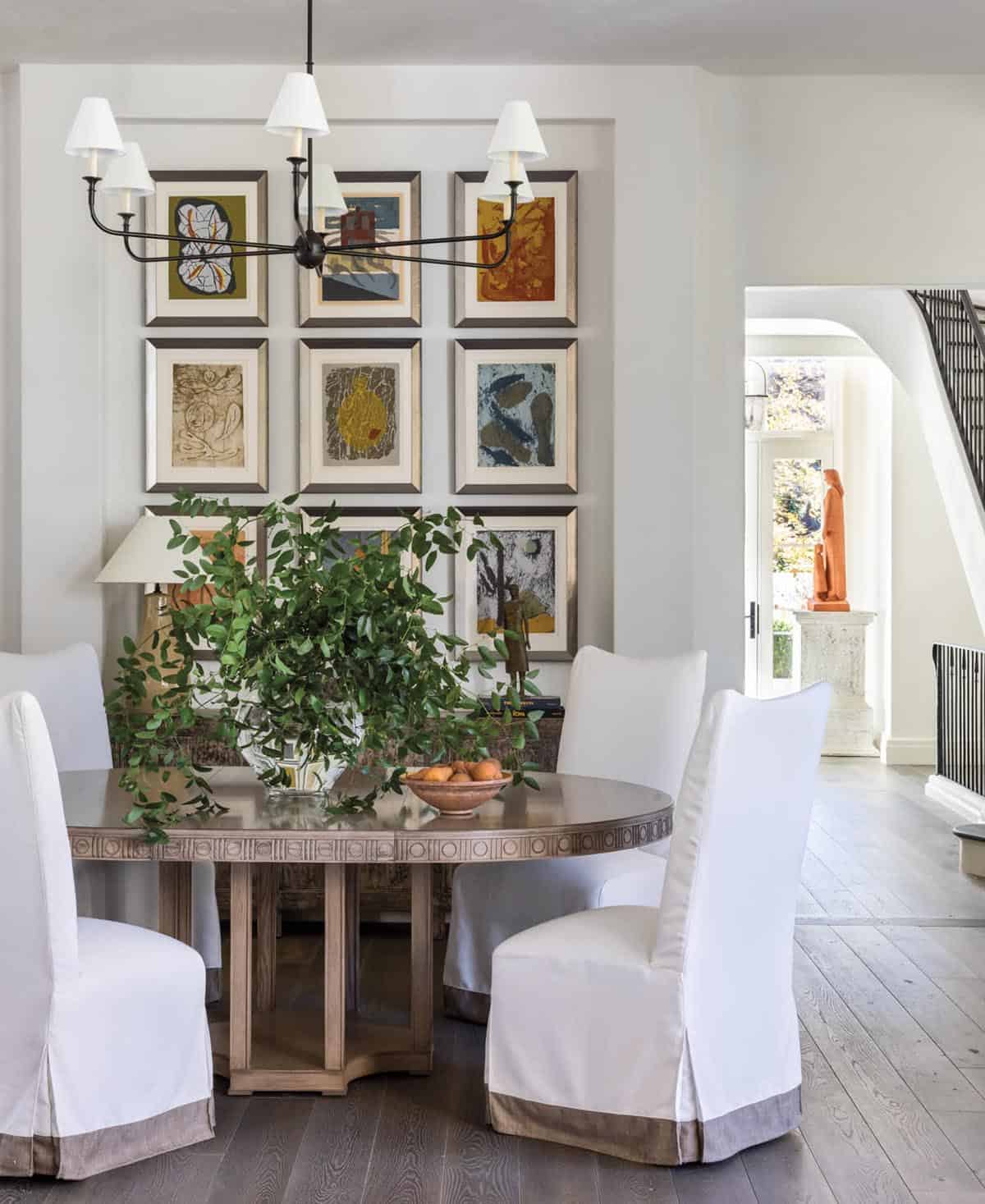 Formal dining room with round pedestal table, slipcovered chairs, and nine-piece gallery wall