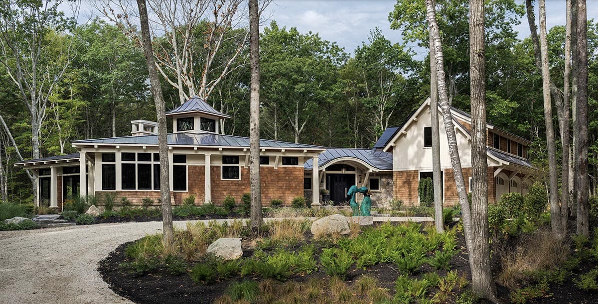Cedar shingle and stone retreat with standing seam metal roof and cupola nestled in Maine woodland