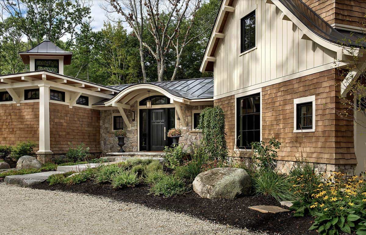 Close-up of cedar shingle retreat entry with arched metal roof portico, stone base, and black front door