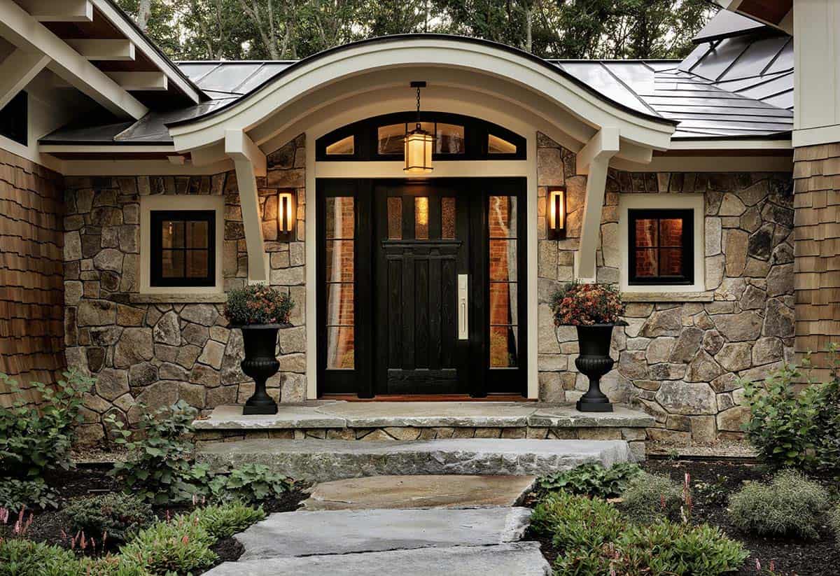 Dramatic arched stone entry portico at dusk with black wood front door and lantern pendant lighting