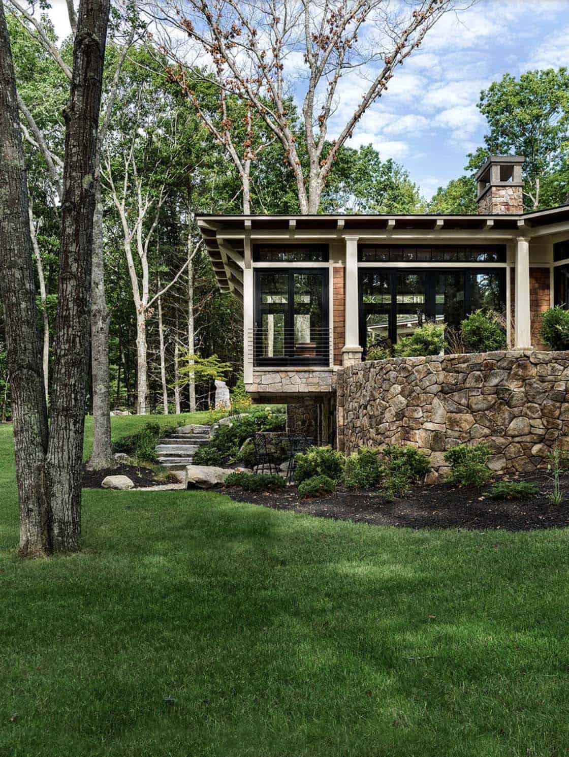 Side view of retreat with cantilevered great room, stone retaining wall, and mature woodland setting