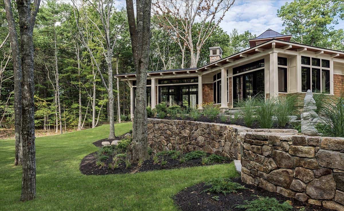 Rear garden view of Maine retreat with curved stone retaining walls, tiered plantings, and black-framed windows