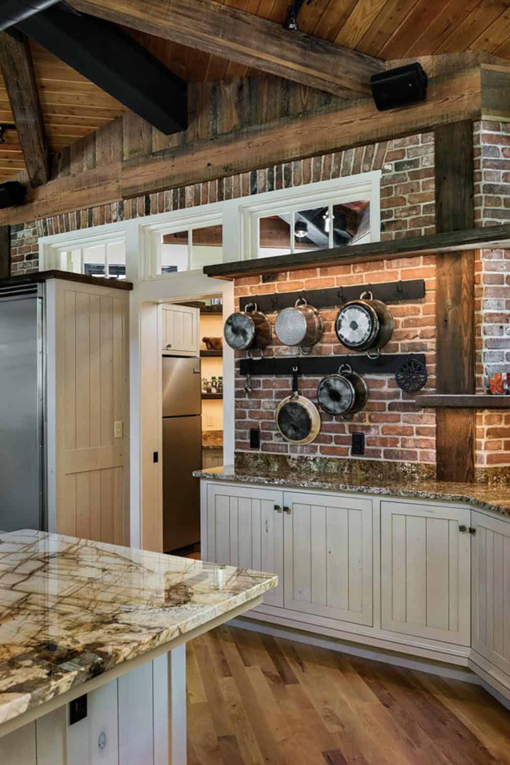 Kitchen detail showing pot rack on reclaimed brick wall, granite countertops, and walk-in pantry entry