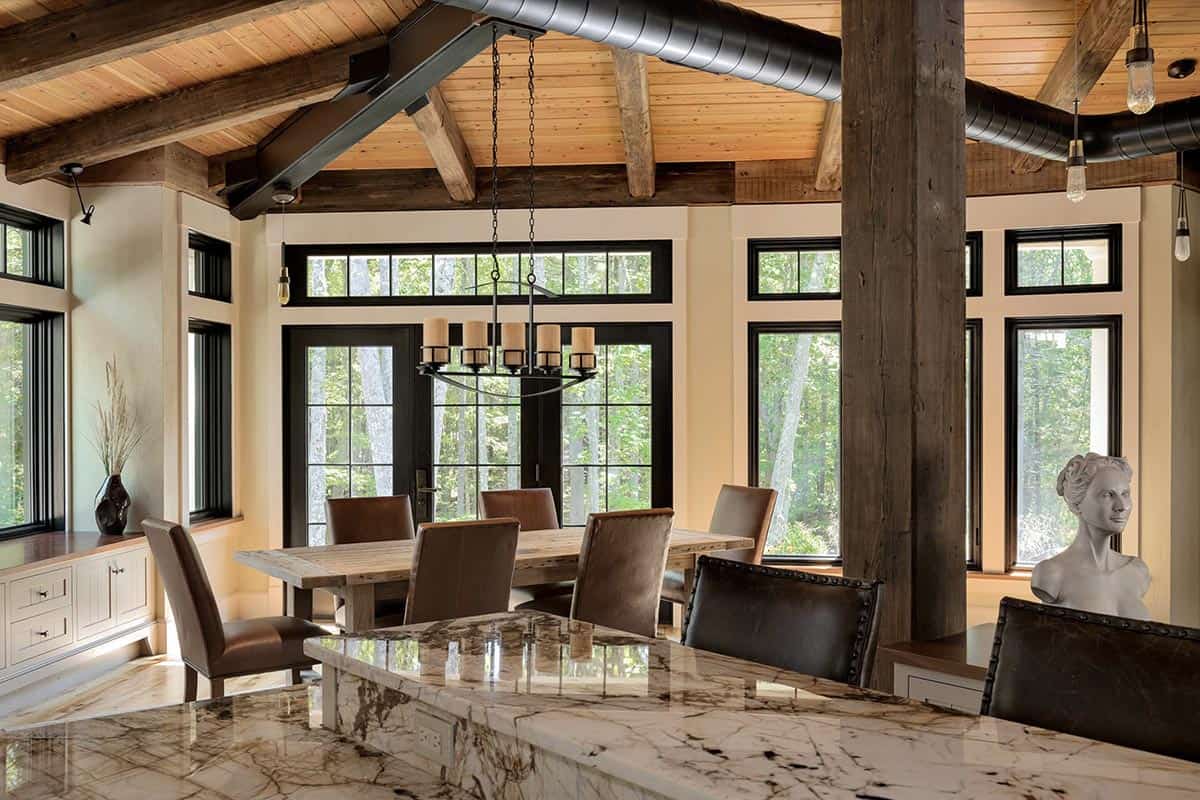 Dining area with reclaimed timber post and beam ceiling, iron chandelier, and walls of black-framed woodland views