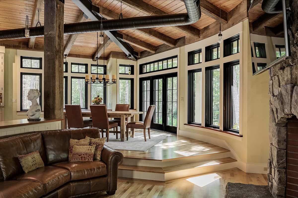 Open living and dining space with cantilevered stepped floor, leather sofa, stone fireplace, and woodland views