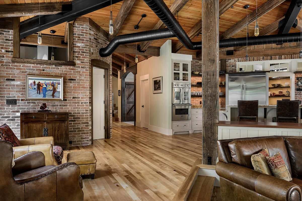 Open plan living area with reclaimed brick walls, exposed ductwork, timber post and beam, and Viking range beyond
