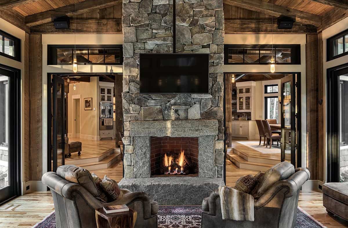 Close-up of floor-to-ceiling granite stone fireplace with lit fire and leather armchairs in cantilevered great room