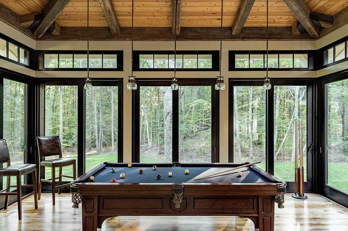 Billiard room with antique pool table, timber beam ceiling, and wraparound black-framed woodland windows