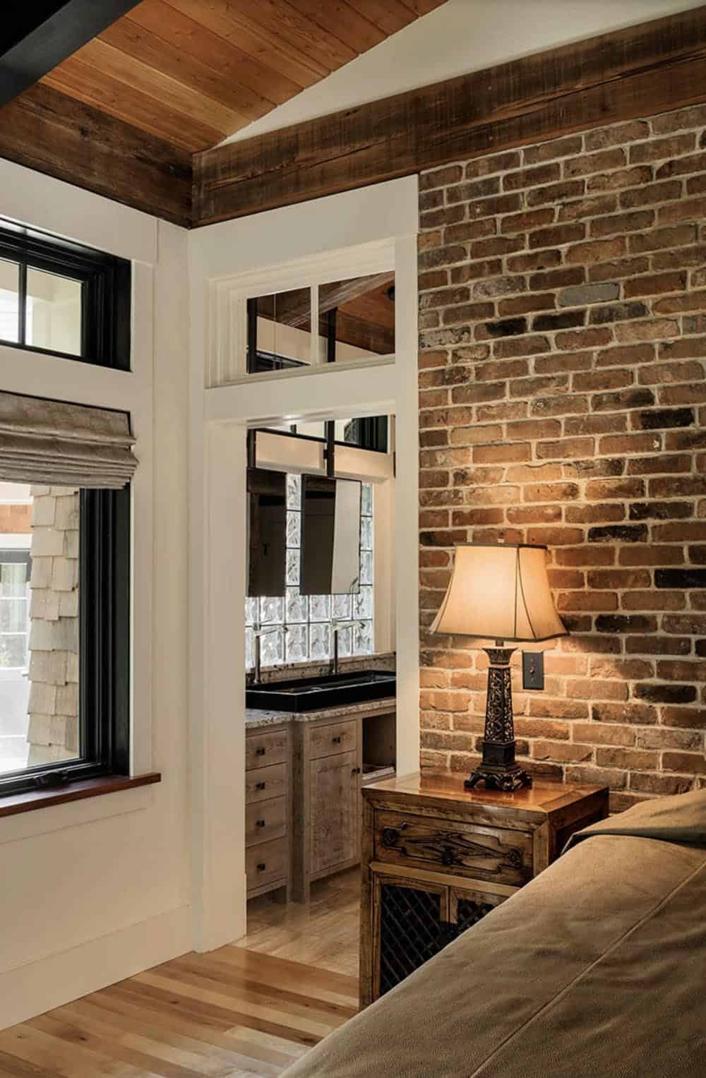 Main bedroom detail showing reclaimed NYC brick accent wall, bedside lamp, and view into en suite bathroom