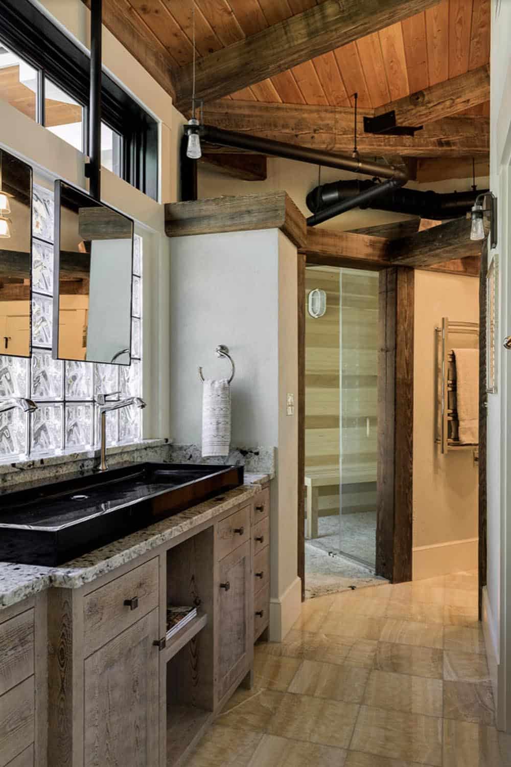 Main bathroom with reclaimed wood vanity, black granite trough sink, glass block window, and walk-in sauna beyond