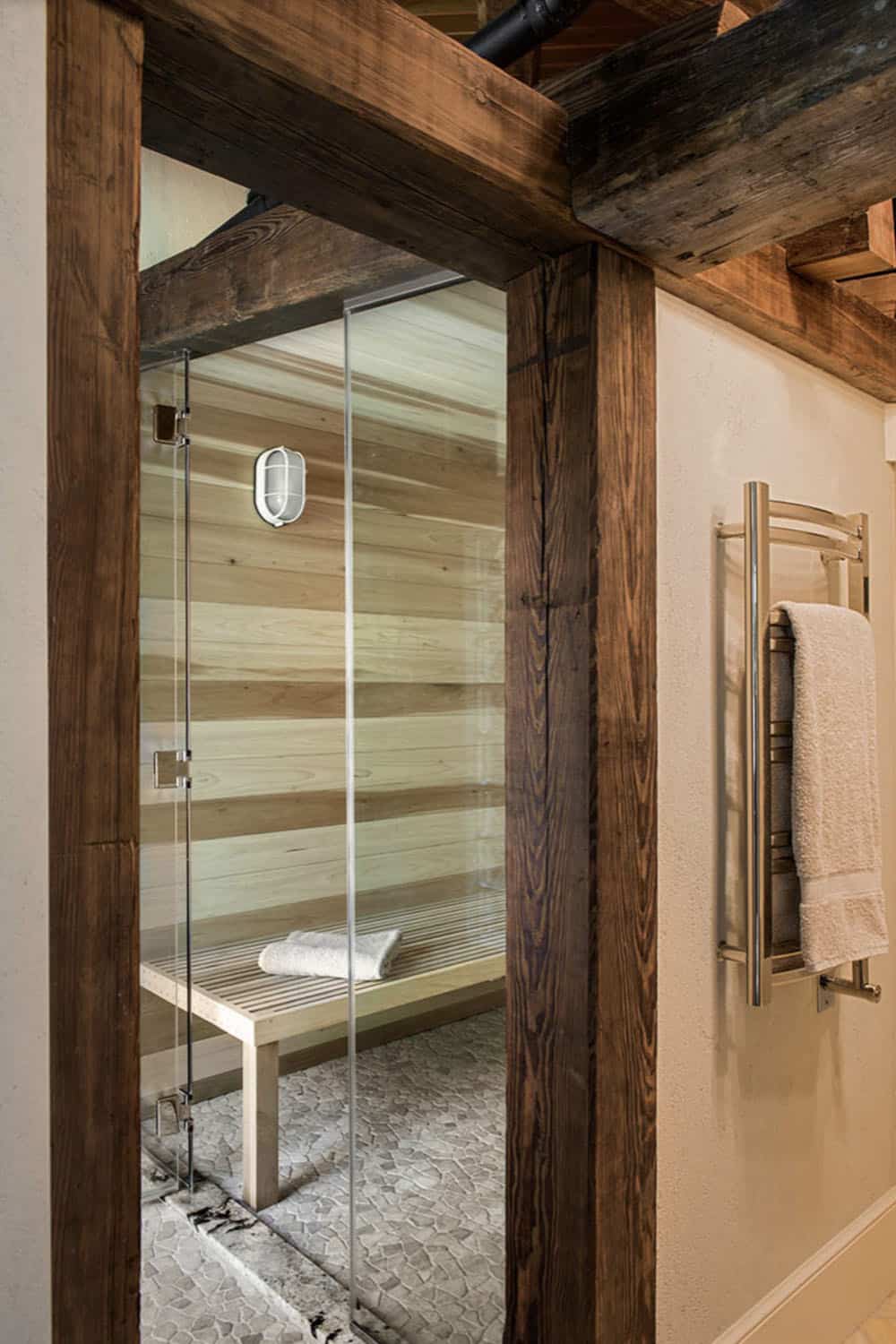 Custom poplar wood sauna with glass door framed in reclaimed timber posts and pebble stone floor