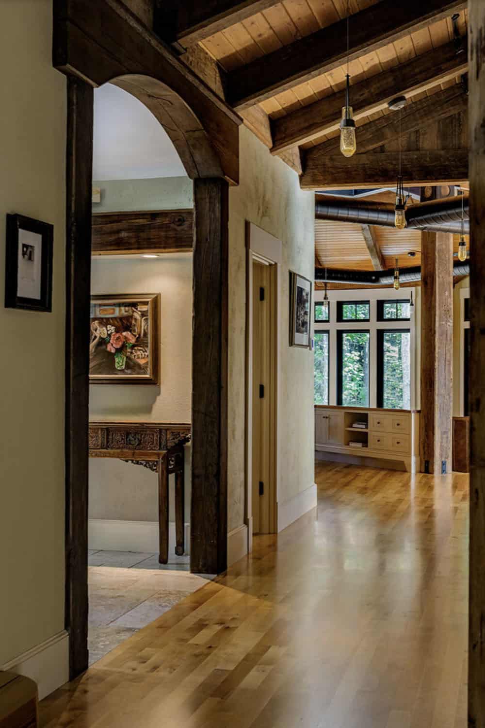 Interior hallway with reclaimed timber arched doorway, hardwood floors, pendant lights, and art collection display