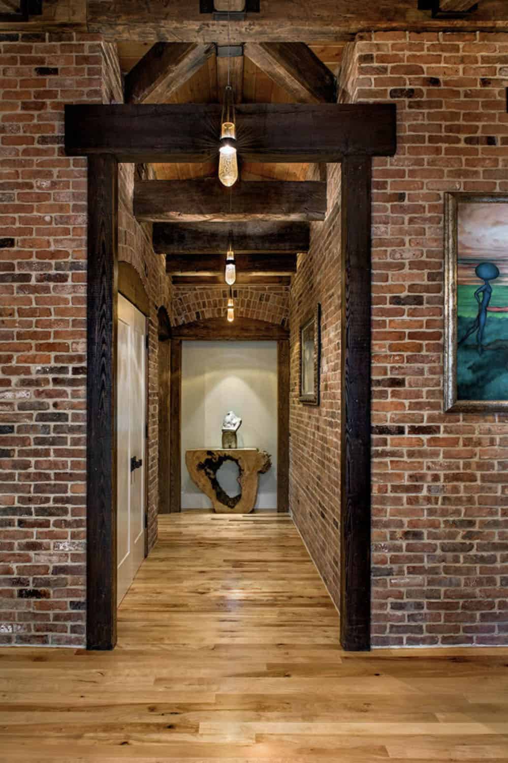 Dramatic NYC reclaimed brick corridor with timber post portal, Edison pendant lights, and live-edge console beyond