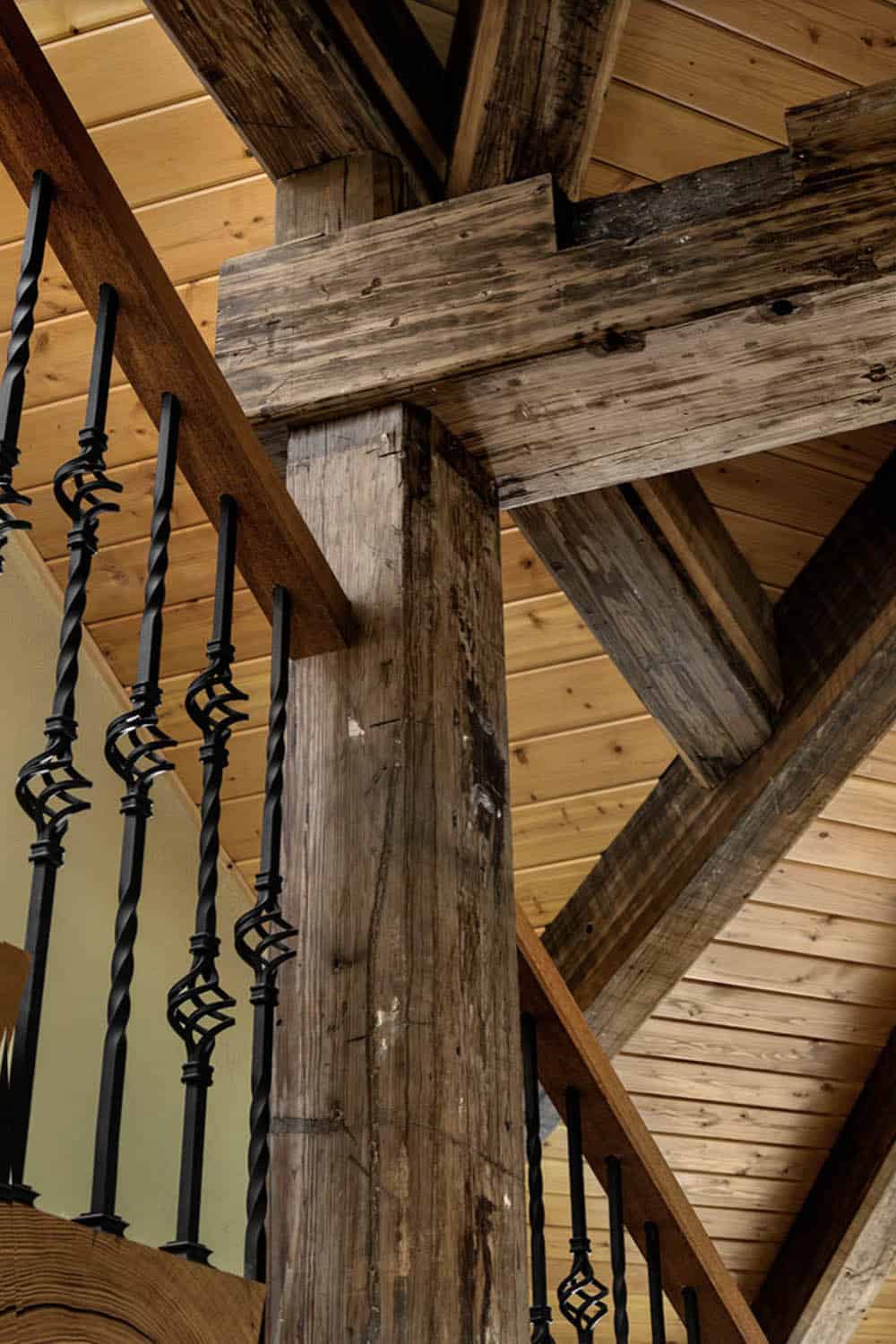 Close-up detail of reclaimed timber post and beam junction with decorative wrought iron stair balusters