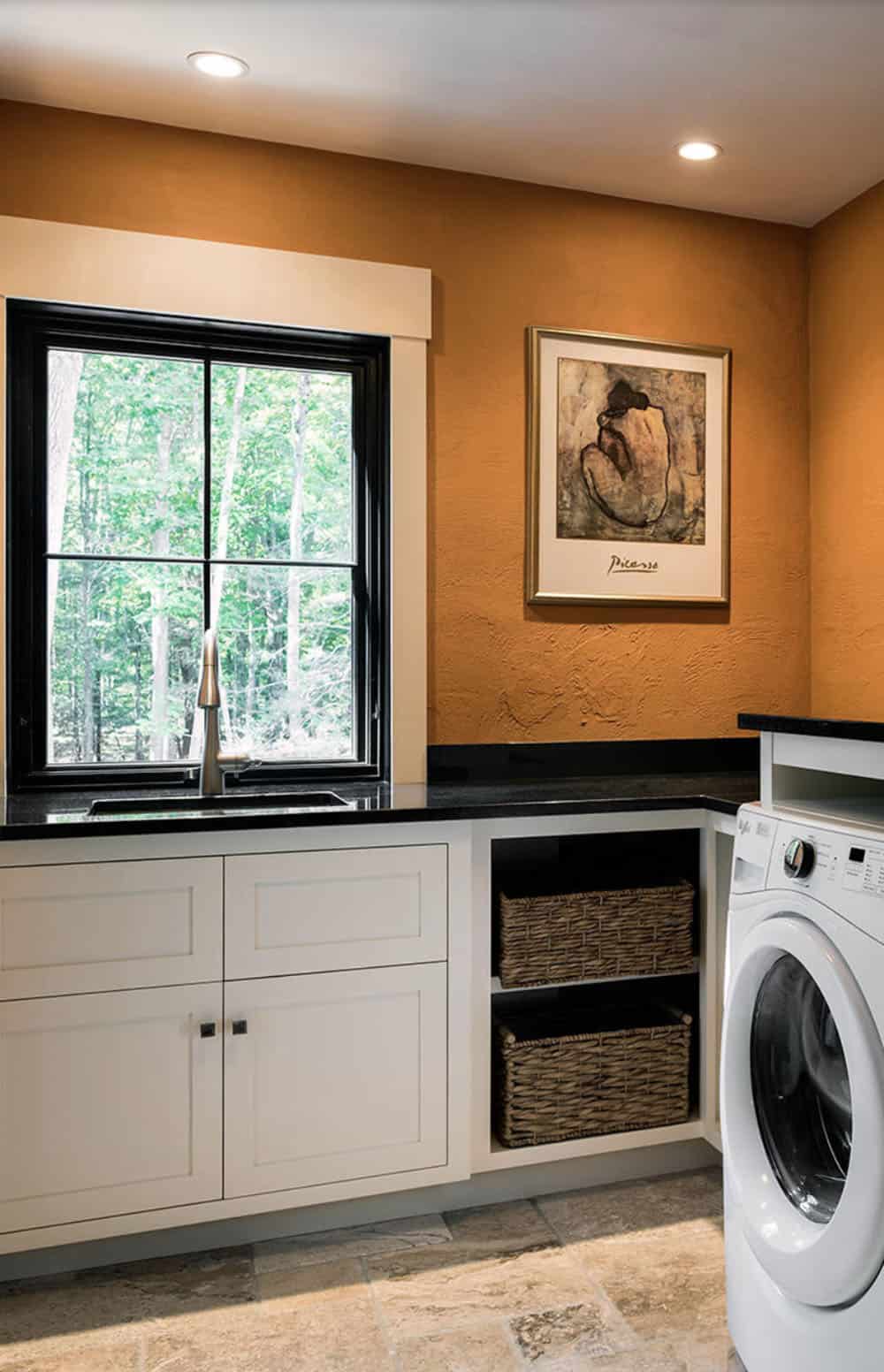 Laundry room with terracotta textured walls, white shaker cabinetry, black granite countertop, and woodland window