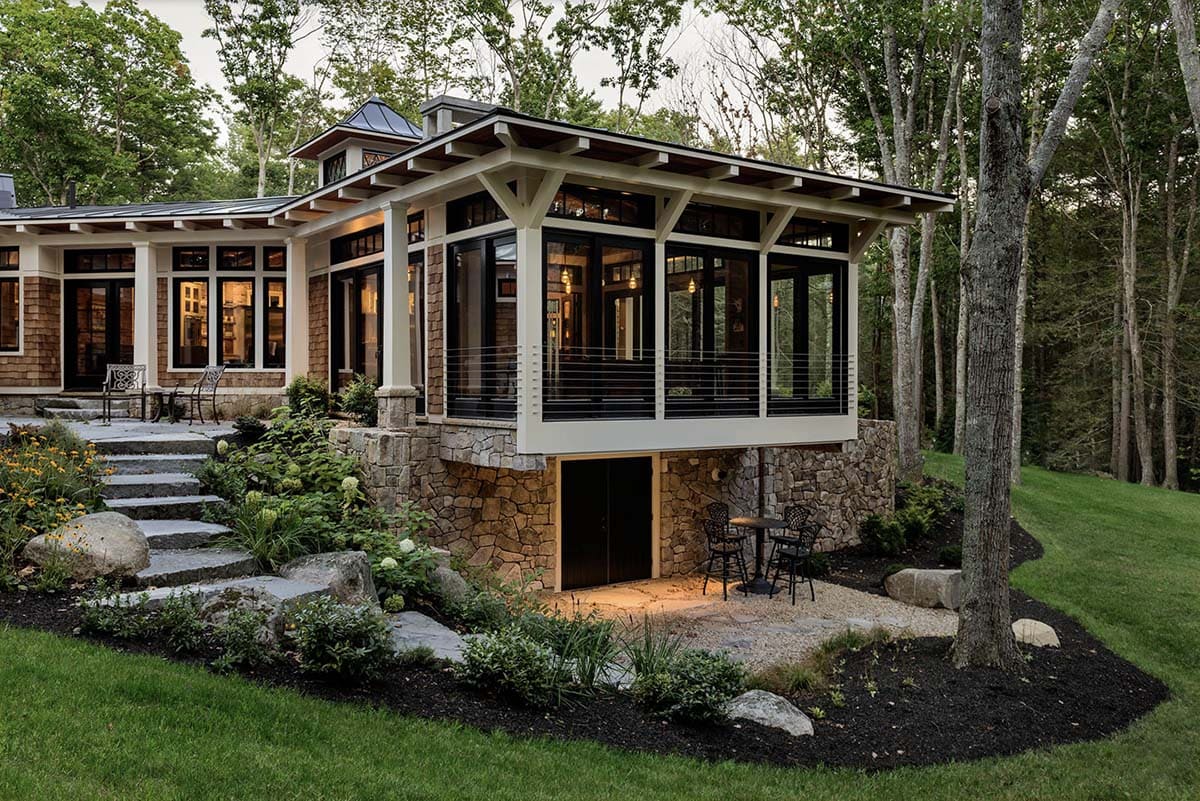 Dusk view of cantilevered great room pavilion with stone base, lower patio bar seating, and tiered garden steps