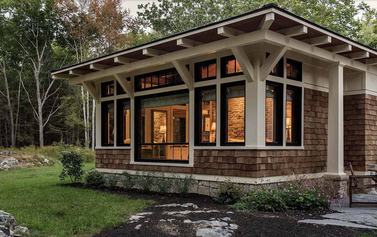 Dusk close-up of cedar shingle master bedroom wing with walls of black-framed windows glowing warmly at twilight