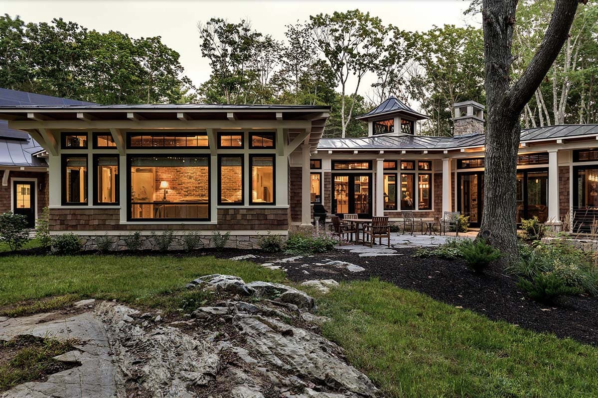Evening rear view of retreat with glowing bedroom and kitchen wings, stone patio dining, and cupola silhouette