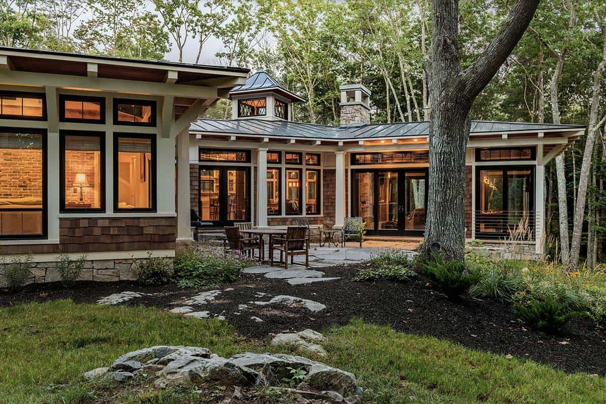 Dusk rear elevation with flagstone patio, teak dining furniture, cupola, stone chimney, and wraparound illuminated glazing