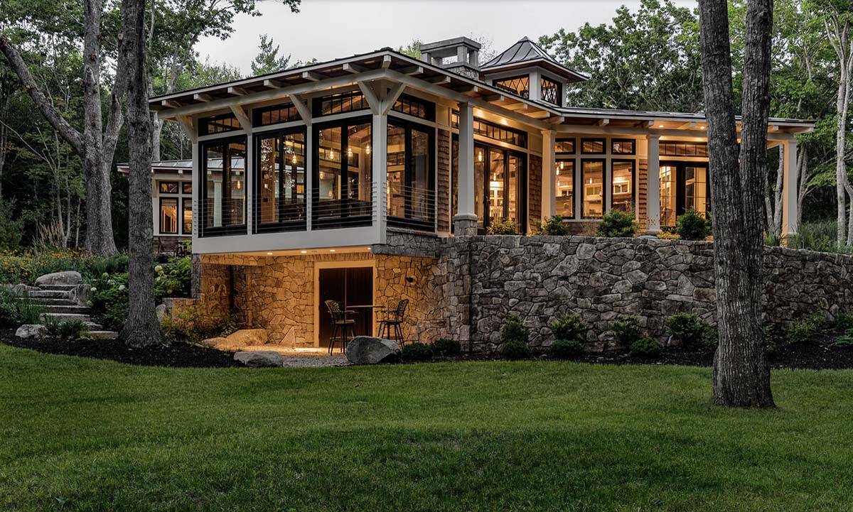Full dusk rear view of retreat showing cantilevered glazed pavilion, stone retaining wall, lower patio, and cupola above