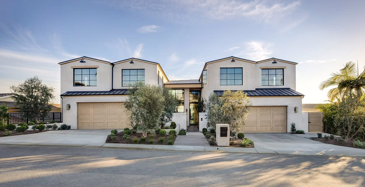 Coastal contemporary home exterior with white stucco, black-framed windows, wood garage doors, and Mediterranean landscaping