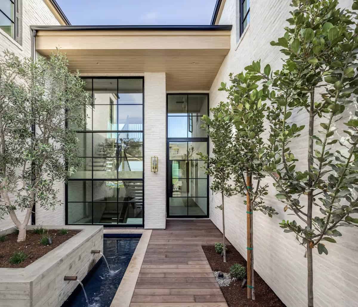 Entry courtyard with floor-to-ceiling steel-framed glass doors, linear water feature, and olive trees