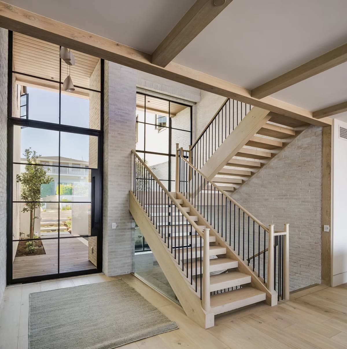 Foyer with open-tread oak staircase, black iron balusters, and steel-framed glass entry doors