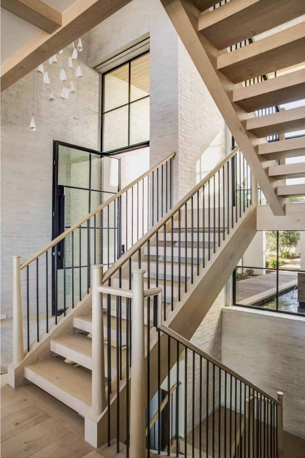 Double-flight staircase with light oak treads, black metal railings, and white brick walls
