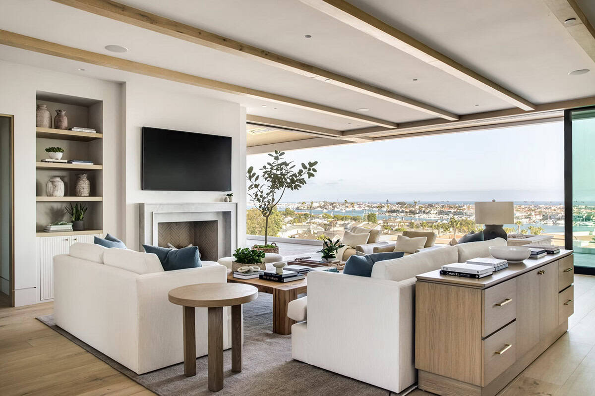 Bright living room with white sofas, oak beams, built-in shelving, fireplace, and panoramic harbor views
