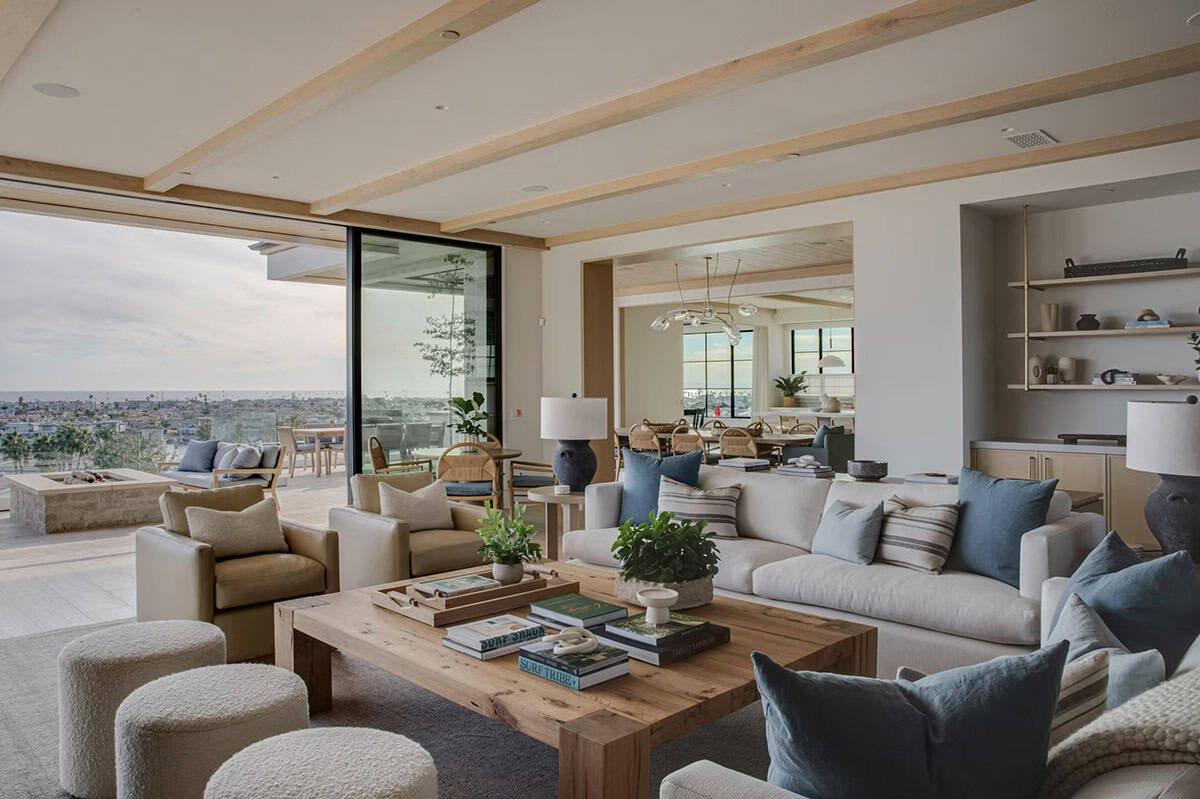 Open-plan living area with linen sectional, blue accent pillows, rustic coffee table, and ocean views through sliding glass doors