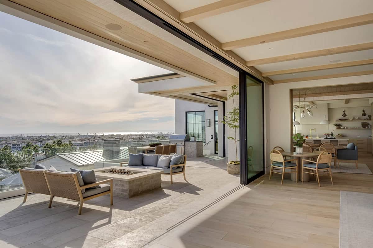 Covered terrace with fire pit seating, glass railing, dining area, and sweeping coastal views