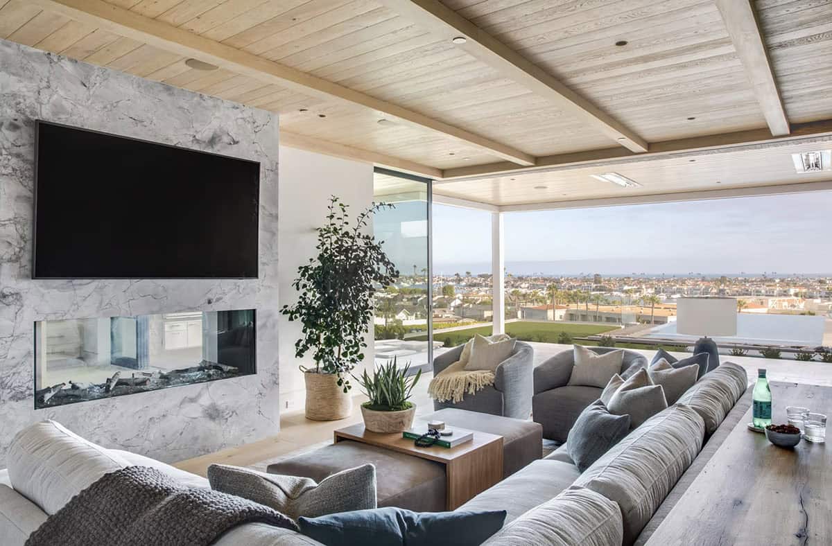 Family room with marble TV wall, linear fireplace, gray sofas, and open glass wall to terrace